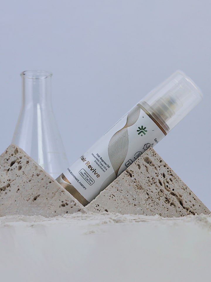 Hair care product bottle labeled 'Revive' on a textured stone surface with a light gray background
